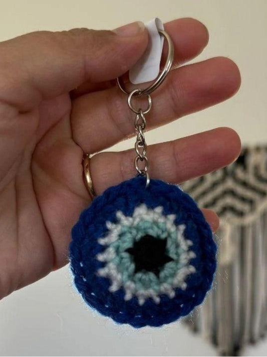 Hand holding an Evil Eye crocheted keychain with a star design.