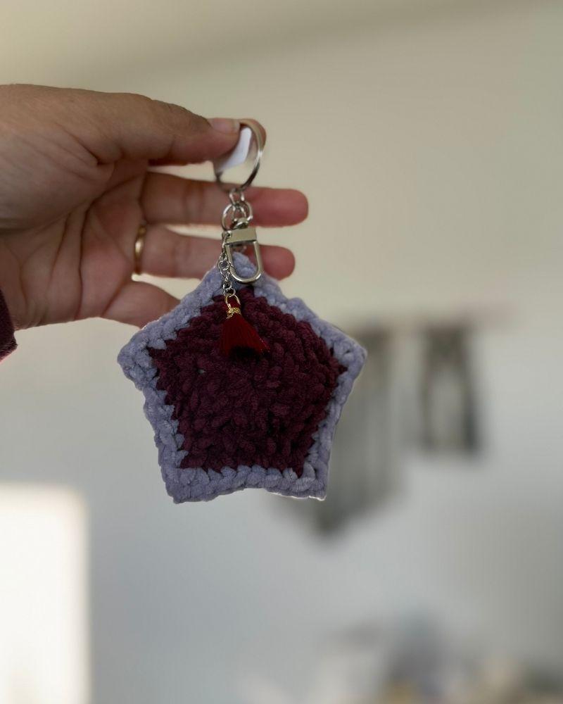 Star-shaped keychain with purple and red colors held by a hand against a blurred background