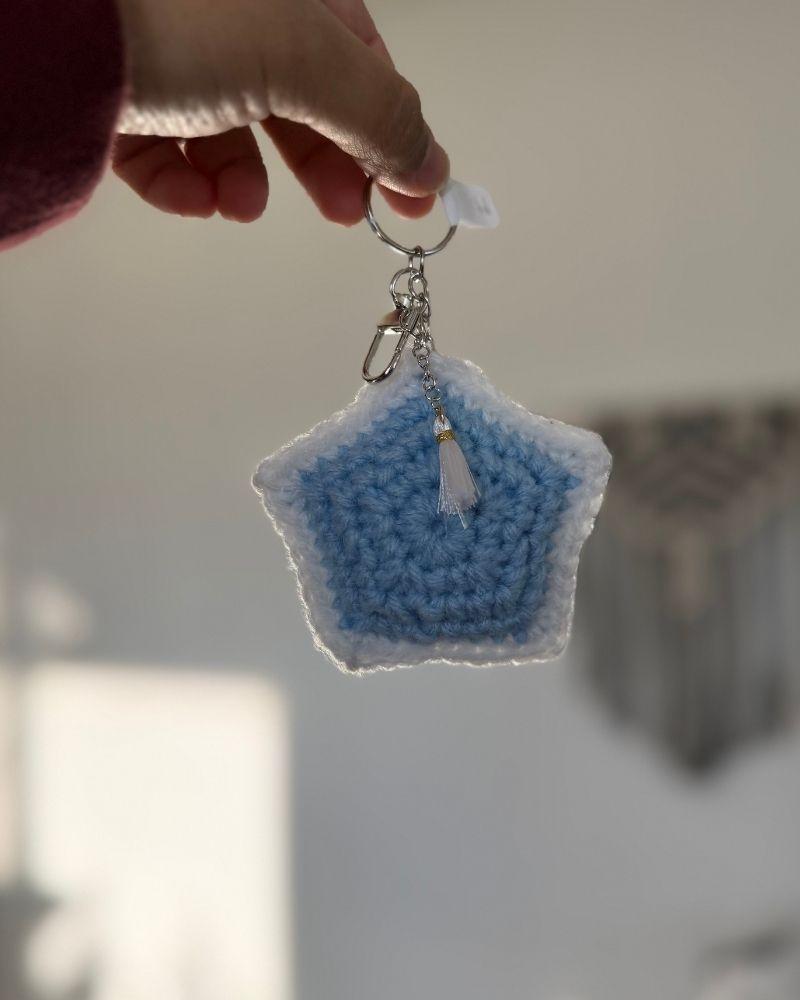 Blue star-shaped keychain held by a hand against a neutral background