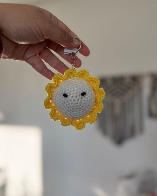 Hand holding a sunflower-shaped keychain with a face against a blurred background