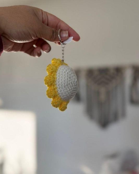 Hand holding a crocheted sunflower keychain against a blurred background